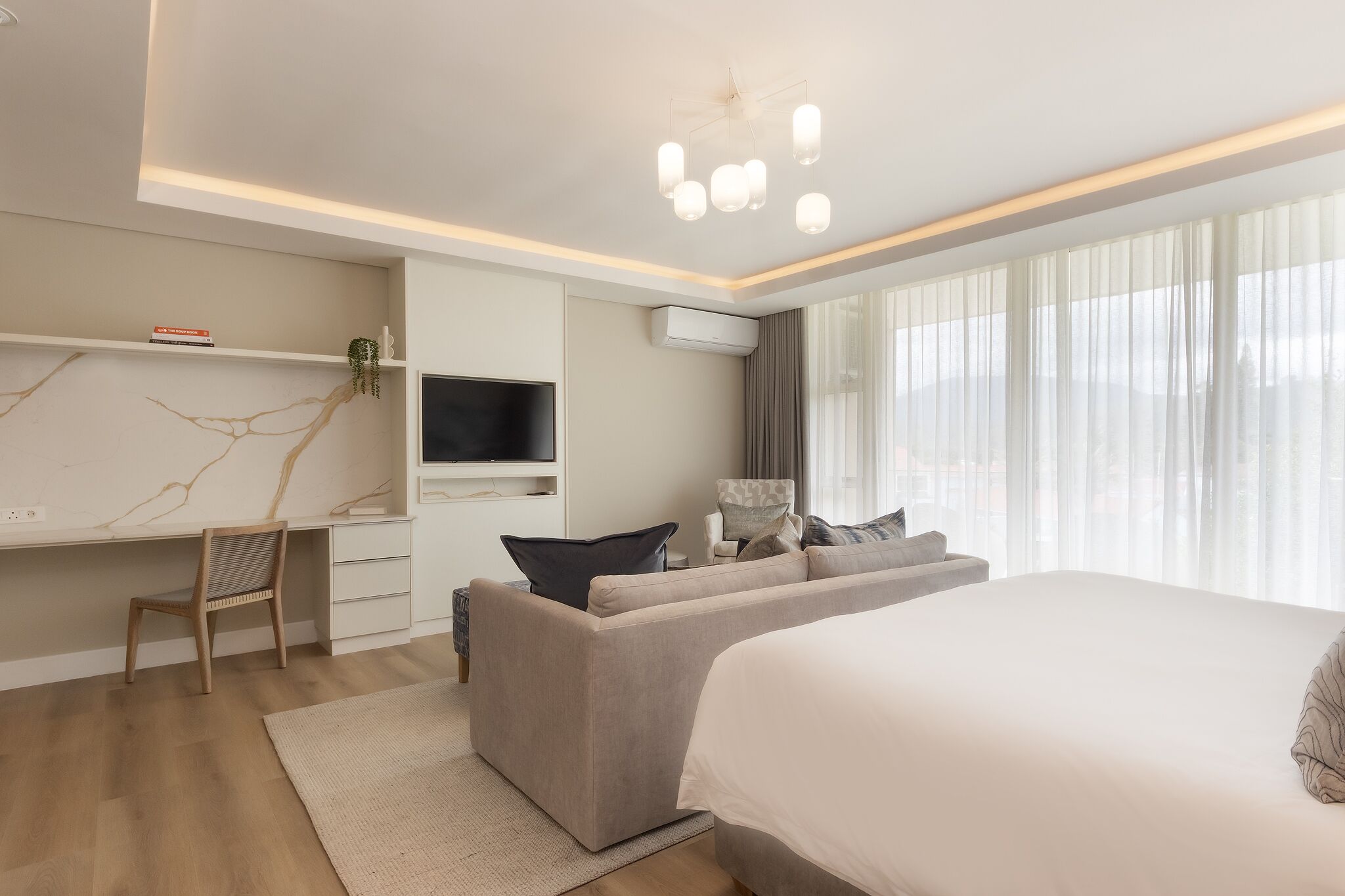 A modern hotel room with a bed, a sofa, a desk, and a TV.