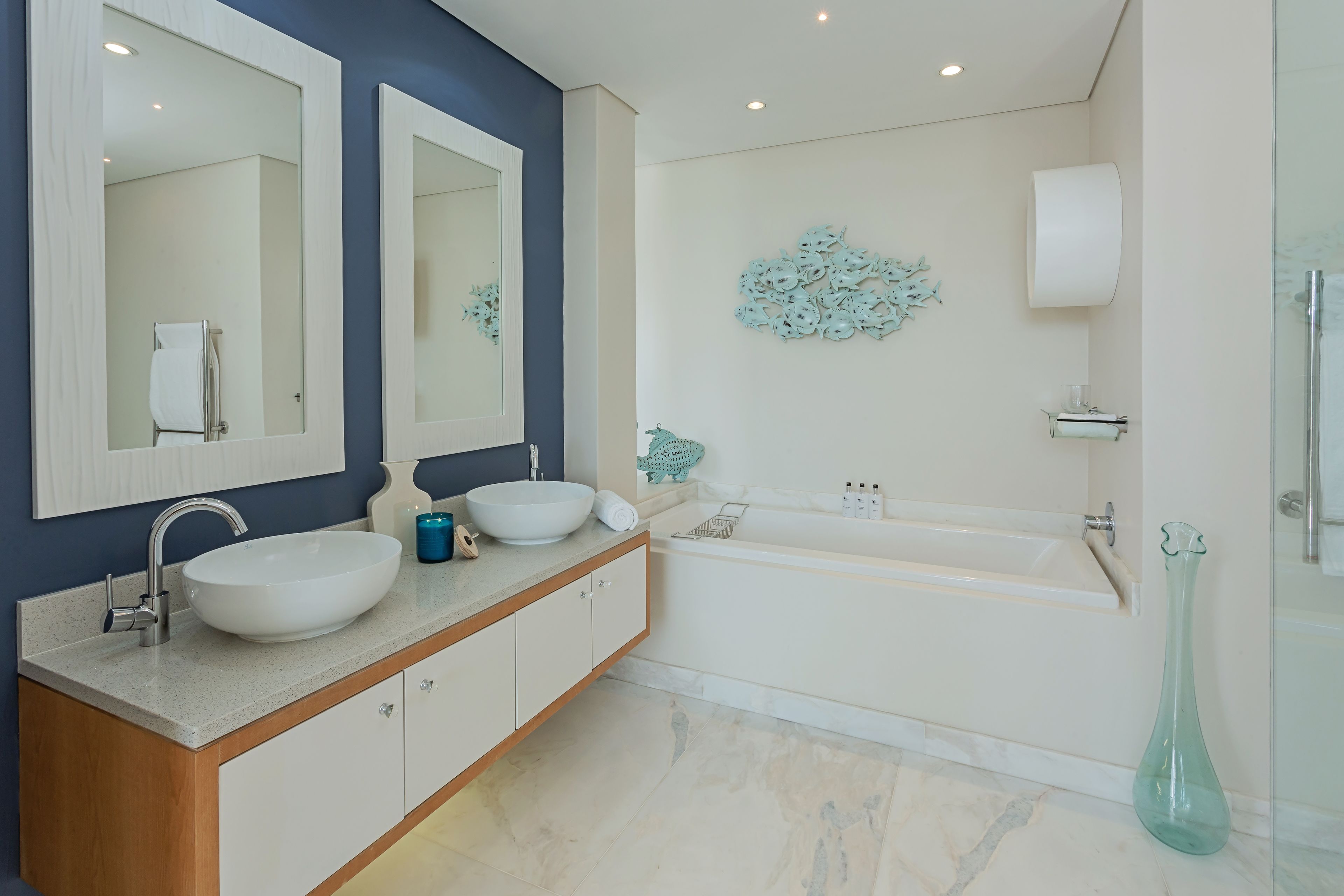 A modern bathroom with a large white sink, two mirrors, a bathtub, and a glass shower enclosure.