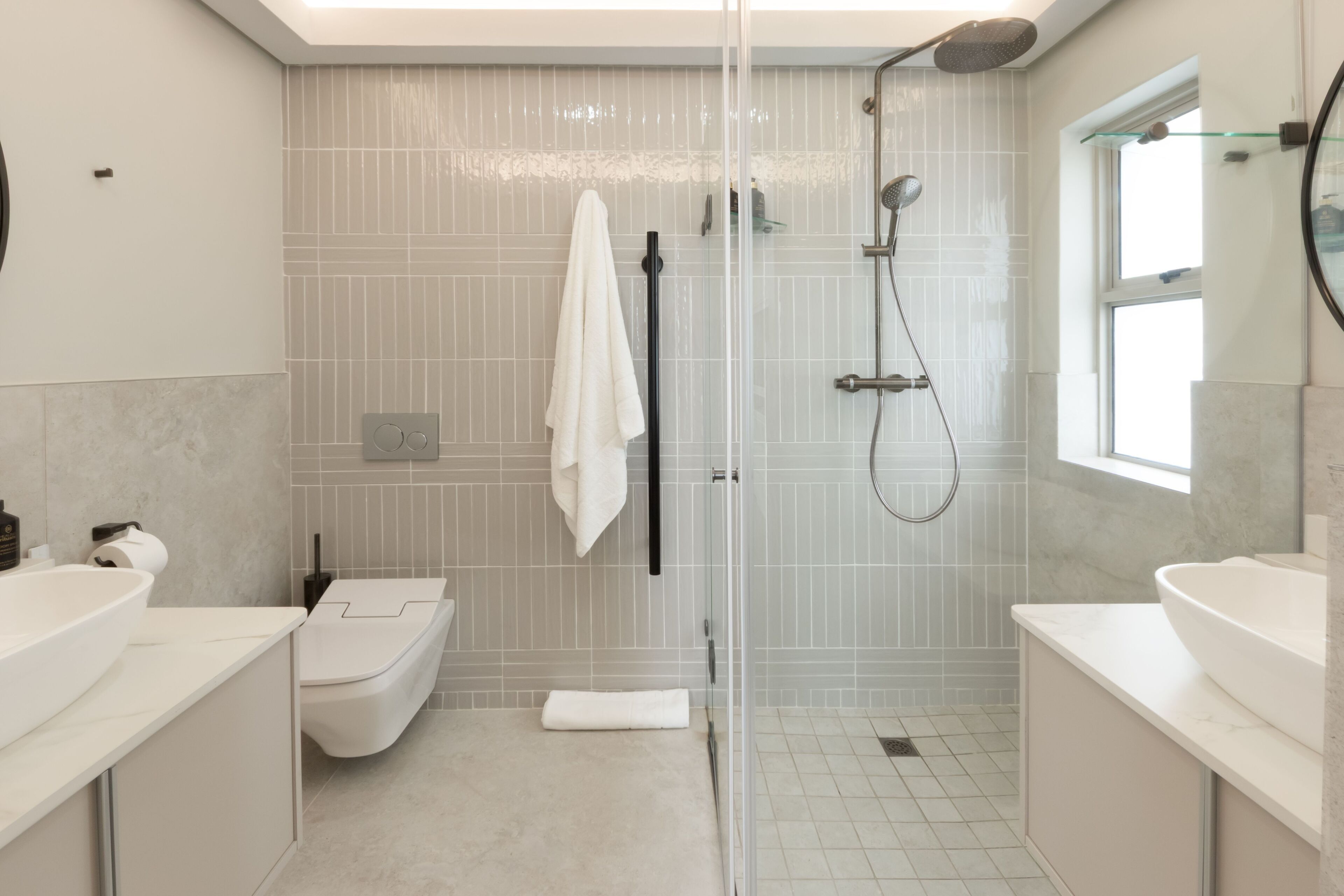 A modern bathroom with a glass-enclosed shower, a toilet, and two sinks.