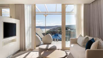 Una sala de estar moderna con un televisor grande, asientos cómodos y vistas a un paisaje costero a través de amplios ventanales.
