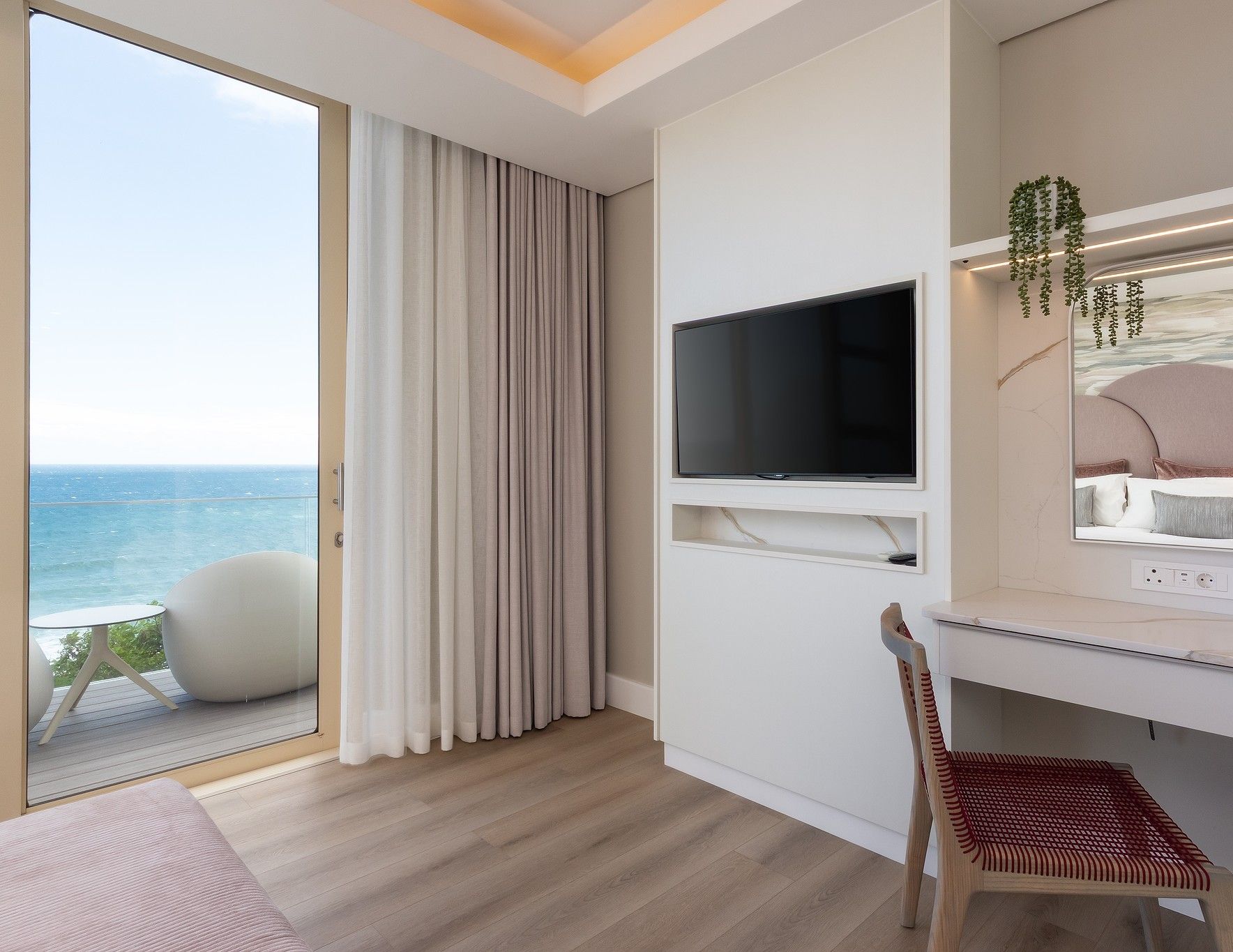A hotel room with a balcony, a TV, a desk, and a chair.