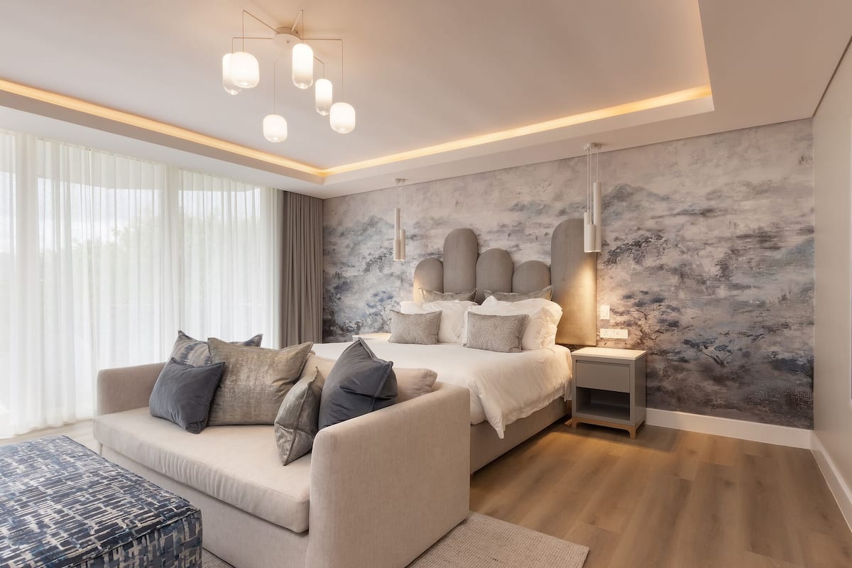A modern bedroom with a large bed, a sofa, a nightstand, and a wall with a textured mural.
