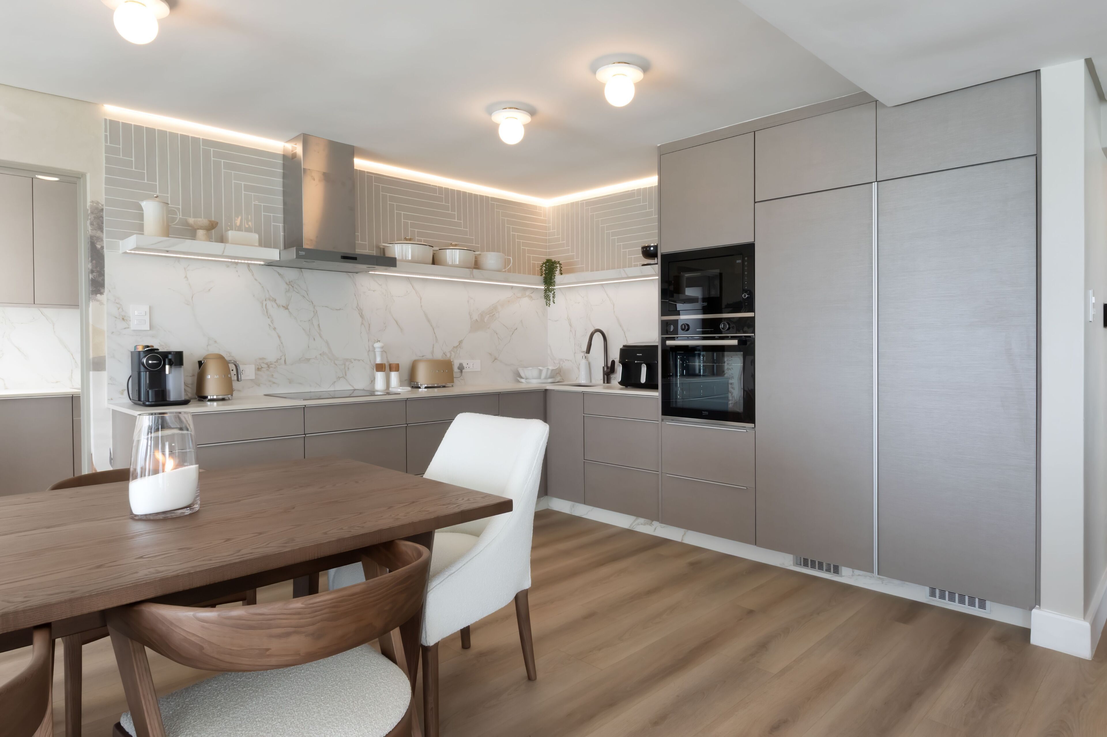 A modern kitchen with marble countertops, stainless steel appliances, and a dining area with a wooden table and white chairs.
