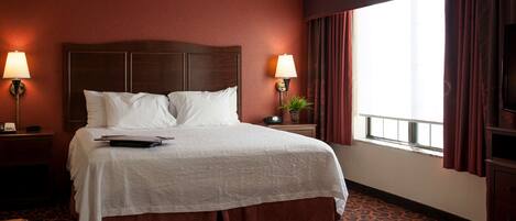 A hotel room with a large bed, two bedside lamps, a TV, and a window with curtains.