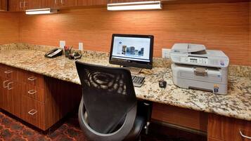 A kitchen with wooden cabinets, a granite countertop, a computer, a printer, and a chair.