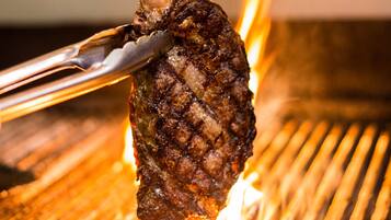 Gros plan d’un steak grillé, maintenu à l’aide de pinces au-dessus d’un gril.