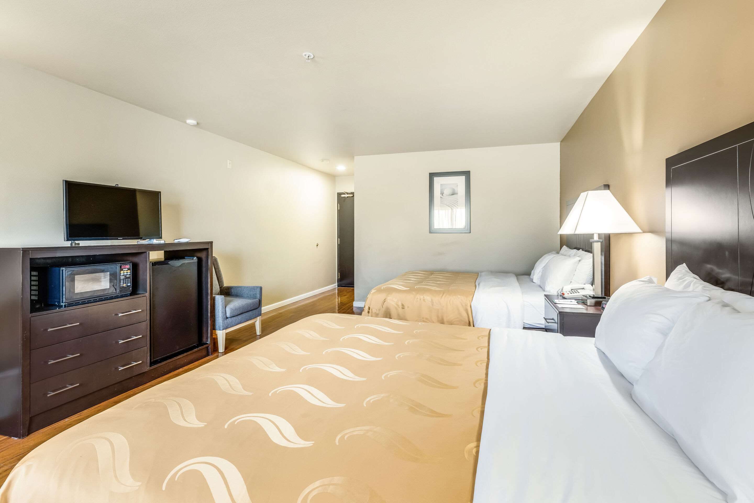 Ein Hotelzimmer mit zwei Betten, einem Fernseher, einer Mikrowelle, einem Schreibtisch und einer Lampe.
