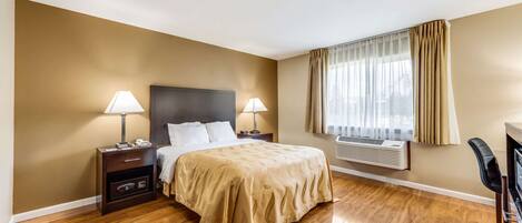A hotel room with a bed, two bedside tables with lamps, a chair, a desk, and a window with curtains.