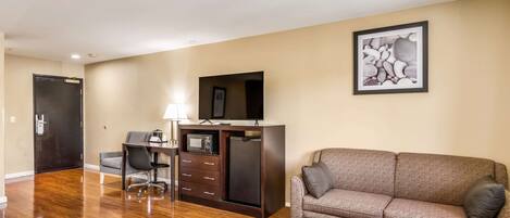 A modern living room with a wooden floor, a sofa, a small table, a TV, and a desk with a lamp.