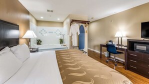 Une chambre d’hôtel comprenant un lit, un bureau, une chaise, une télévision, une lampe de bureau, un peignoir et un espace douche.