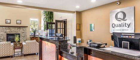 Uma área de recepção de hotel com lareira de pedra, balcão de recepção e uma placa com a inscrição "Quality by Choice Hotels".