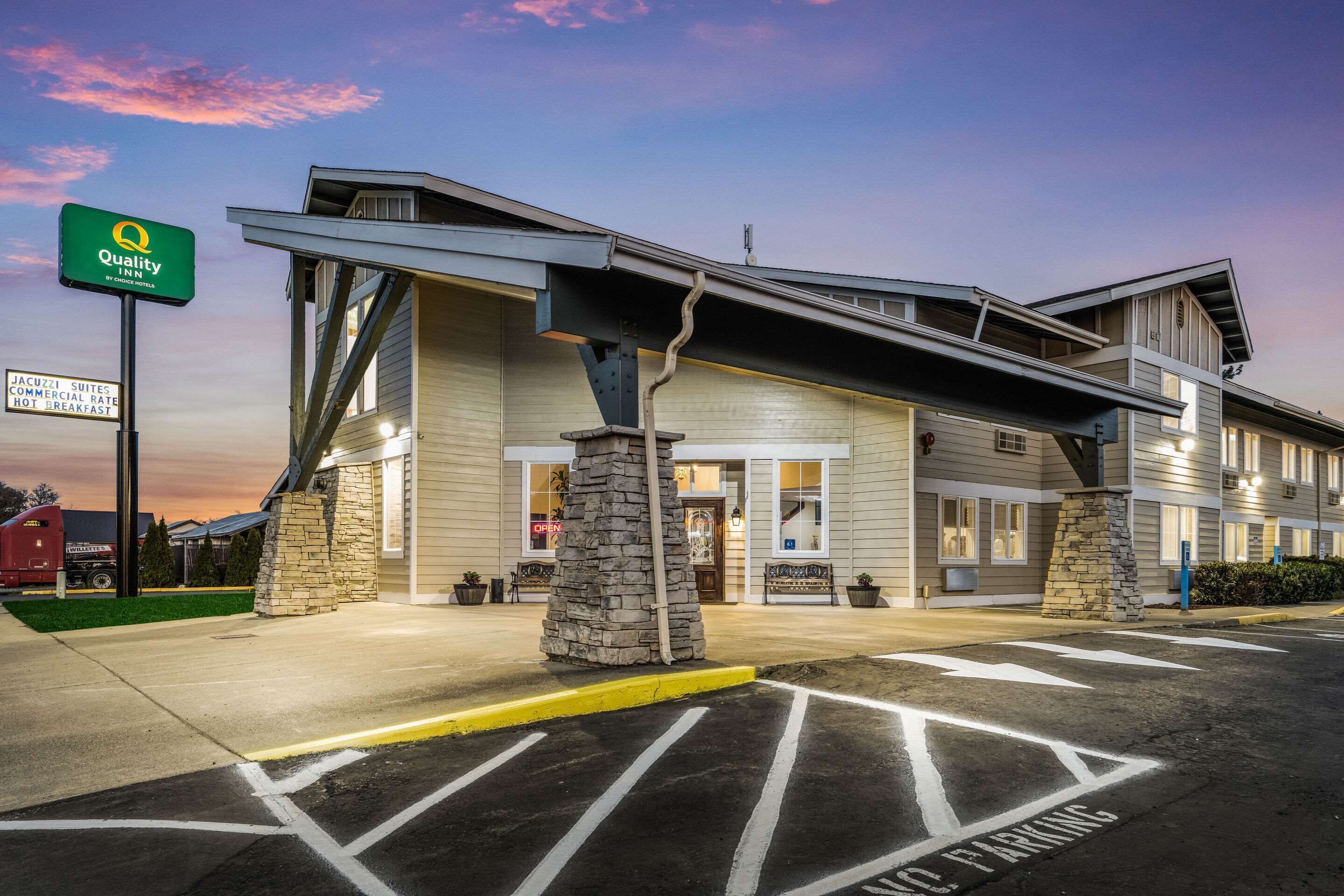 Un hôtel à la façade en pierre, une enseigne « Quality Inn » et un parking avec des flèches indiquant le sens de la circulation.