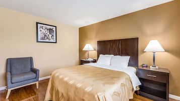 A hotel room with a large bed, two bedside tables with lamps, a chair, and a framed picture on the wall.