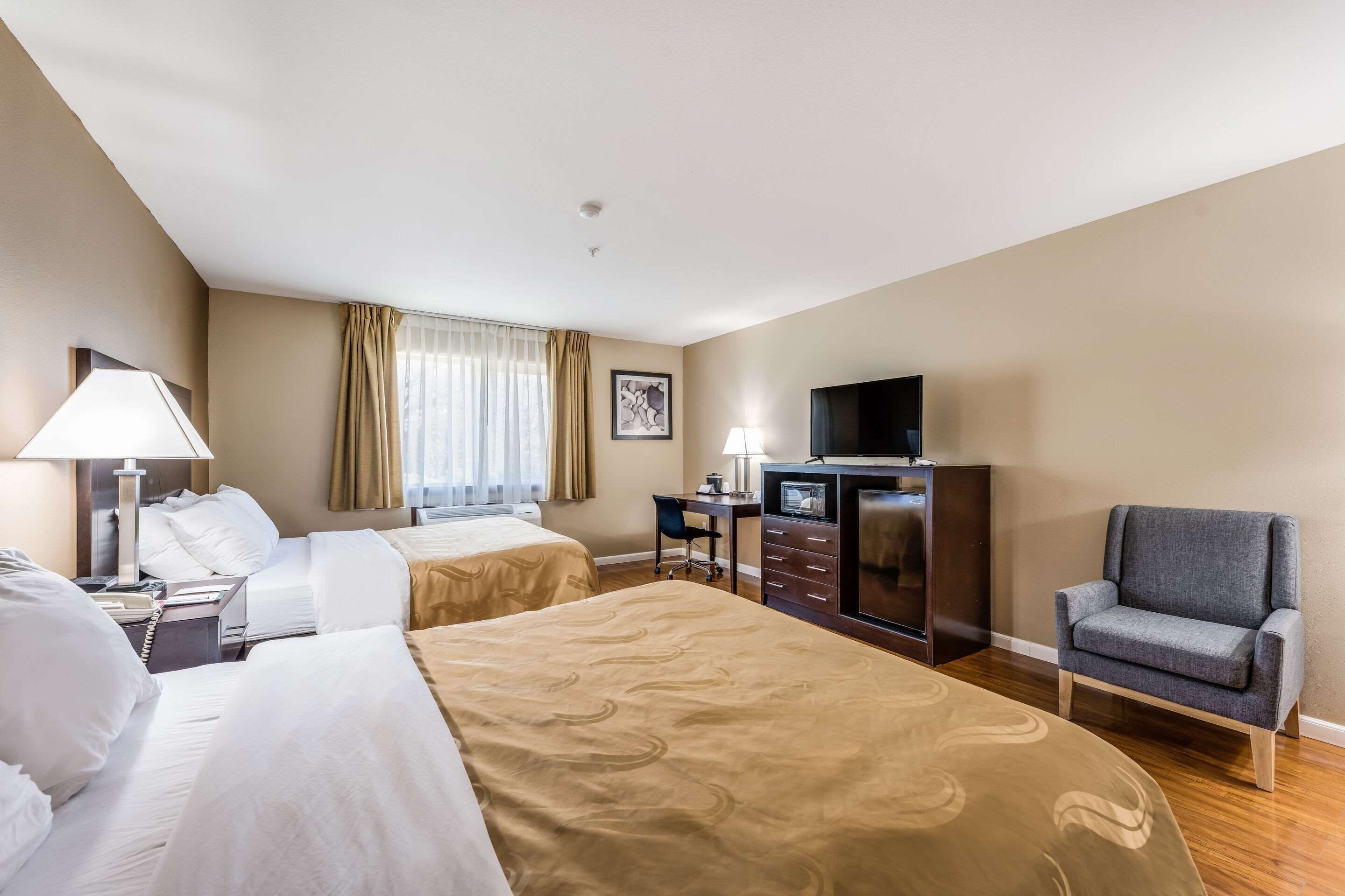 A hotel room with two beds, a desk, a chair, a TV, and a window with curtains.