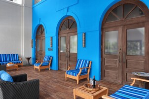 Un área de estar azulada con mobiliario de madera, incluyendo sofás y sillones, y una puerta de madera con panel de vidrio.
