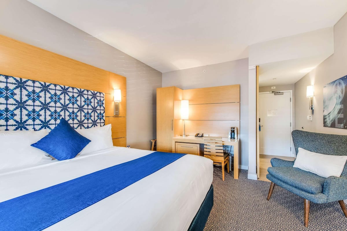 Habitación de hotel con una cama grande, un escritorio, una silla y una puerta que da a otra habitación.