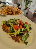 Una mesa de comedor con platos de comida, incluyendo una ensalada y alimentos fritos.
