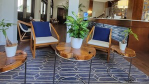 Un vestíbulo con mostrador de recepción, dos sillones azules acolchados y plantas en macetas.