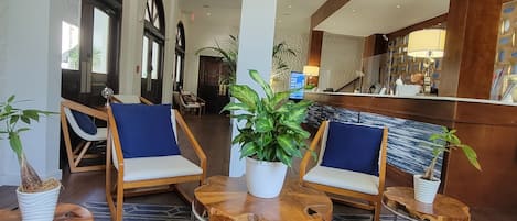 A lobby with a reception desk, two blue cushioned chairs, and potted plants.