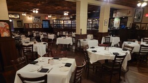 Un restaurante con varias mesas dispuestas para comer, sillas de madera y una zona de bar al fondo.