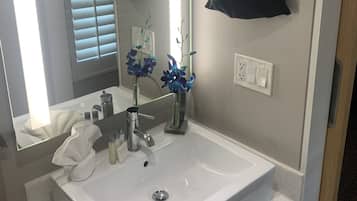 A bathroom with a white sink, a mirror, a towel, and a vase with flowers.