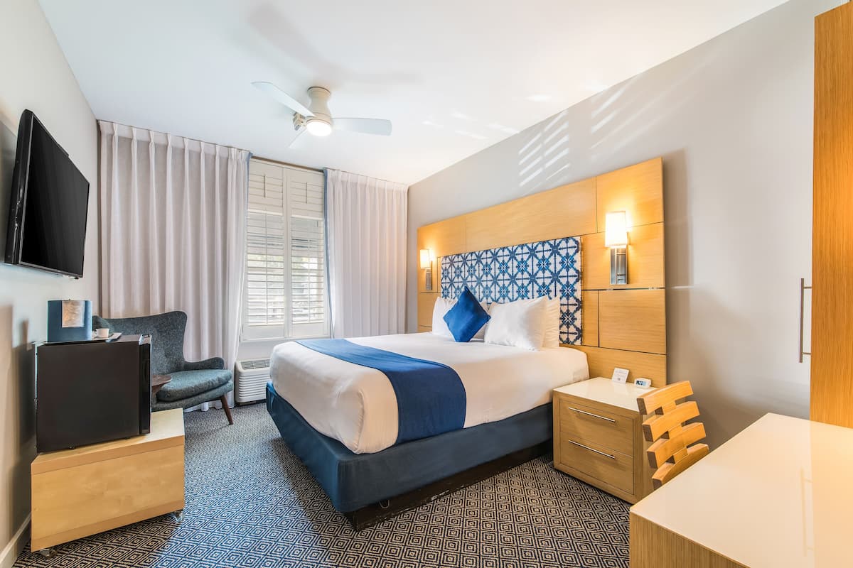 Habitación de hotel con cama, escritorio, silla, televisor y ventilador de techo.