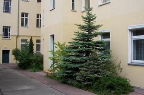 Un edificio residencial con un pequeño árbol de hoja perenne al frente.