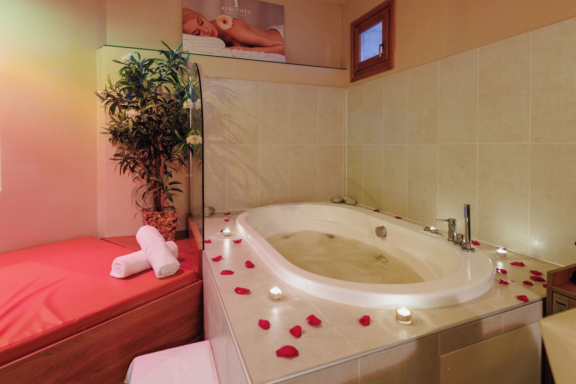 Un baño con una bañera grande, una cabina de ducha de vidrio, una planta en maceta y un banco rojo.