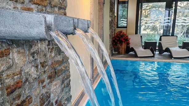 A pool with water cascading from a stone wall, lounge chairs, and a flower arrangement. - Hotel Kastel (Motovun)