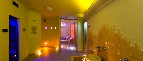 Zona de spa con pared de azulejos, camilla de masaje y una pequeña piscina.
