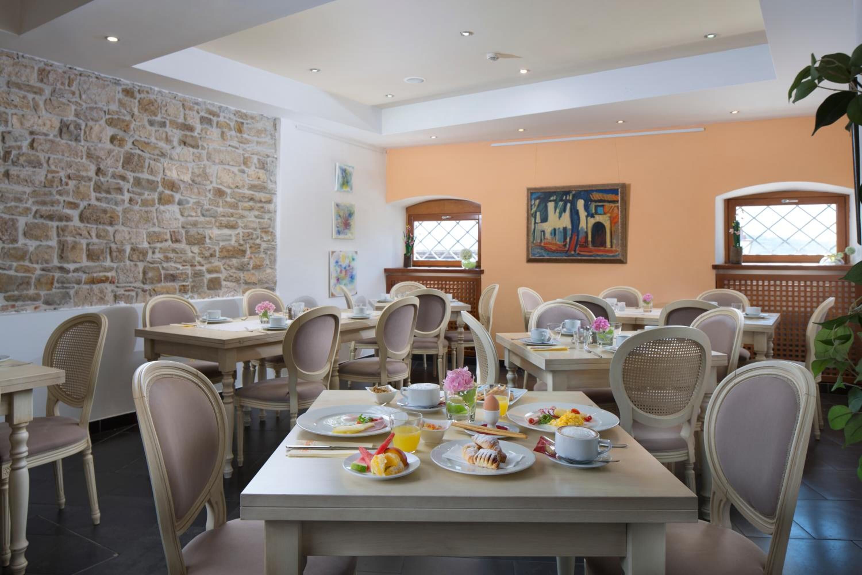 Un espace repas comprenant plusieurs tables et chaises, des murs en pierre et des œuvres d’art accrochées aux murs.