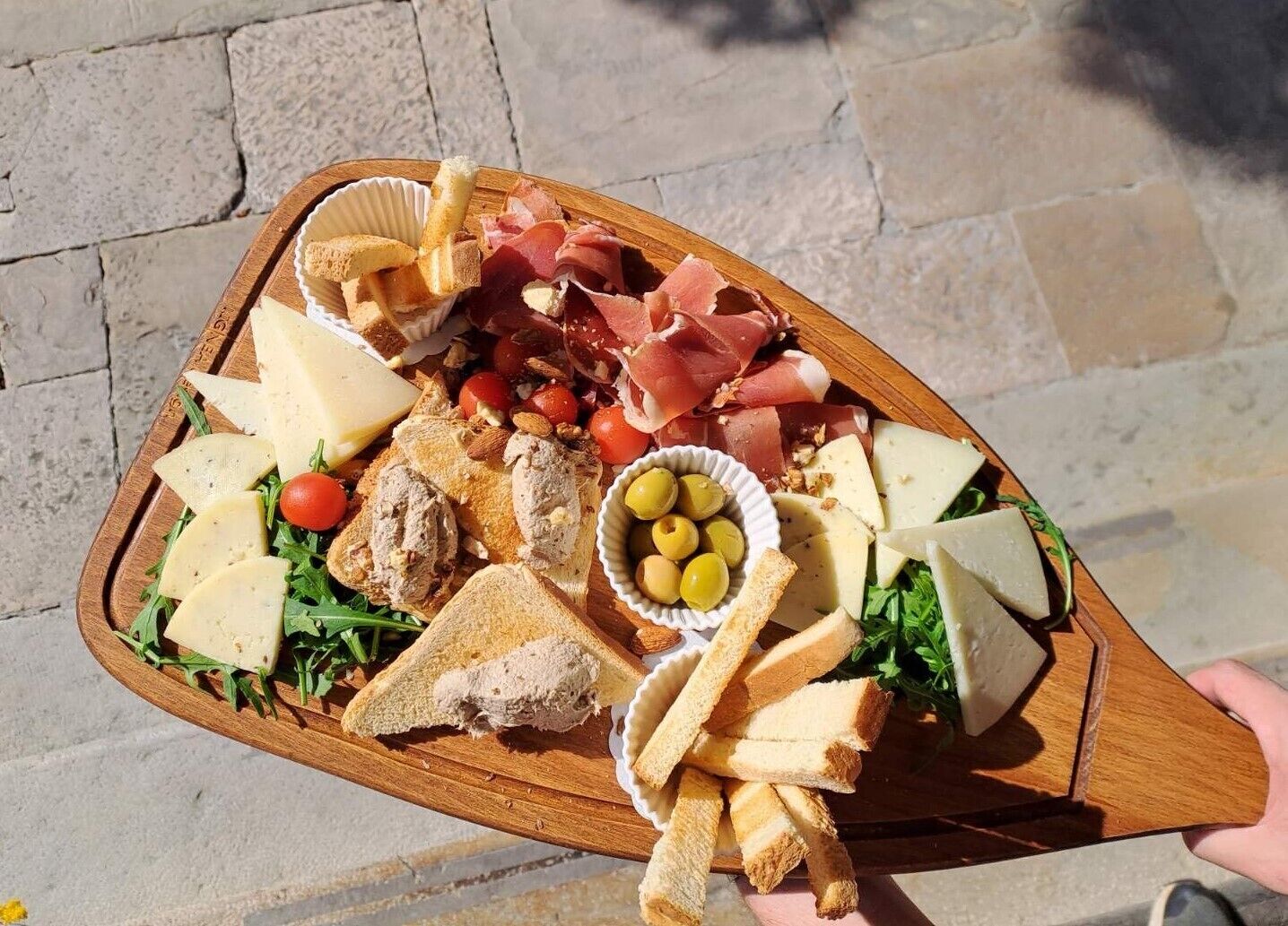 Ein Holzbrett mit verschiedenen Käsesorten, Fleisch, Oliven und Brot.