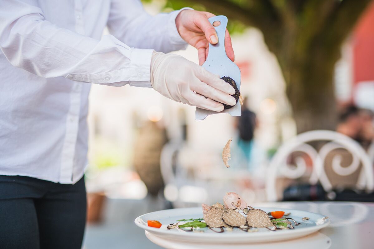 A person in a white shirt and gloves using a blue spatula to serve food on a plate.