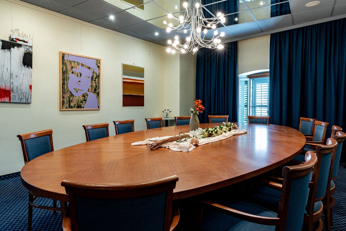 A conference room with a large wooden table, blue chairs, and a chandelier.