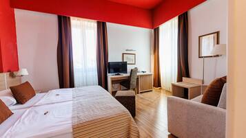 A hotel room with two beds, a desk, a chair, a sofa, and a TV.