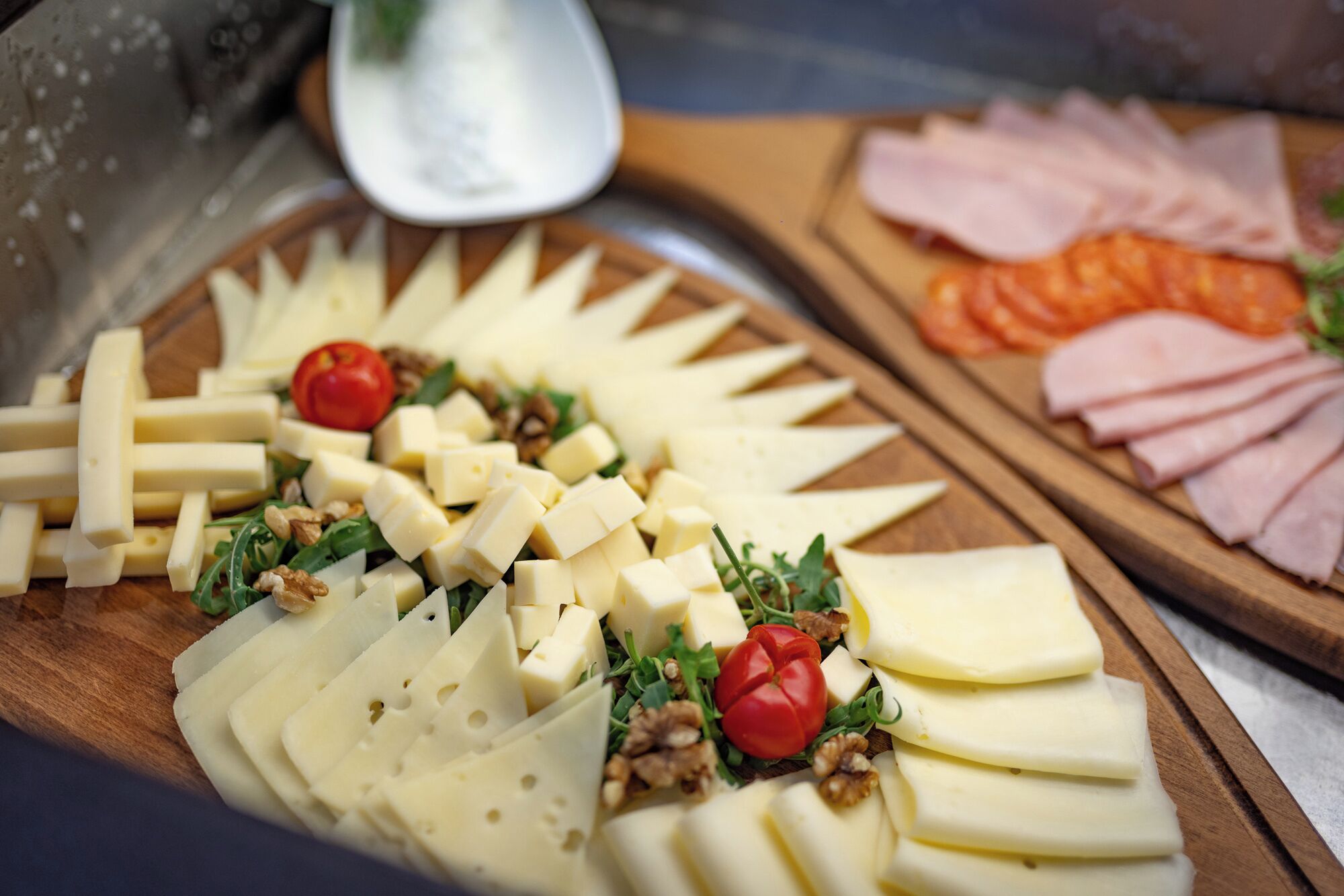 A cheese platter with various cheeses, walnuts, and cherry tomatoes on a wooden board.