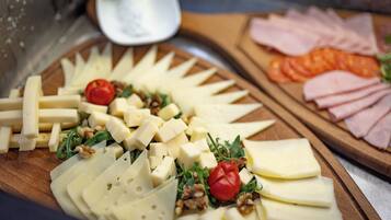 A cheese platter with various cheeses, walnuts, and cherry tomatoes on a wooden board.