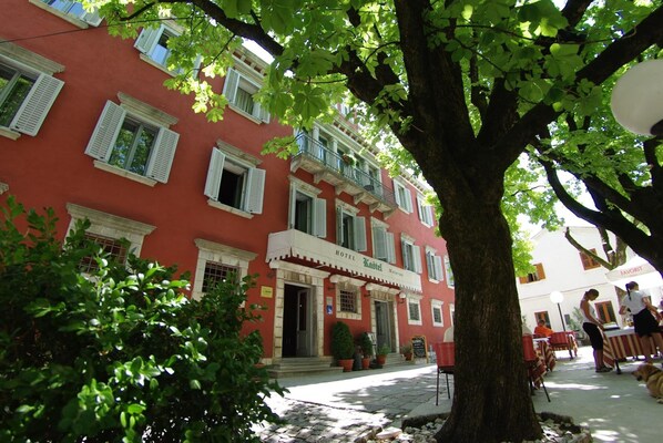 A red building with white shutters, a balcony, and a sign that reads "HOTEL."