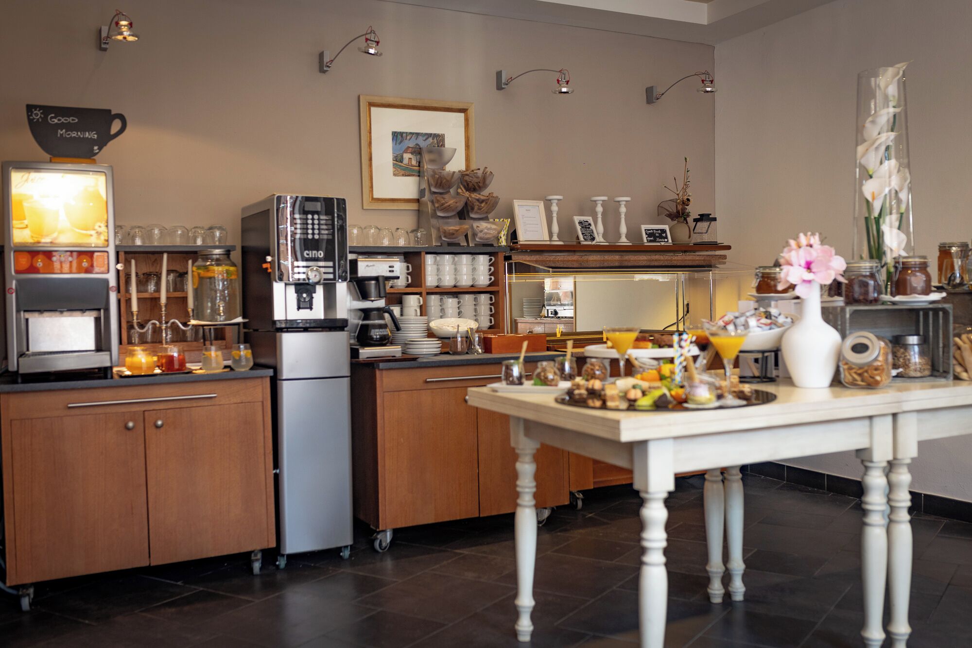 Une cuisine moderne équipée d’une machine à café, d’un coin pour préparer le thé et de divers produits pour le petit-déjeuner, le tout disposé sur le comptoir.