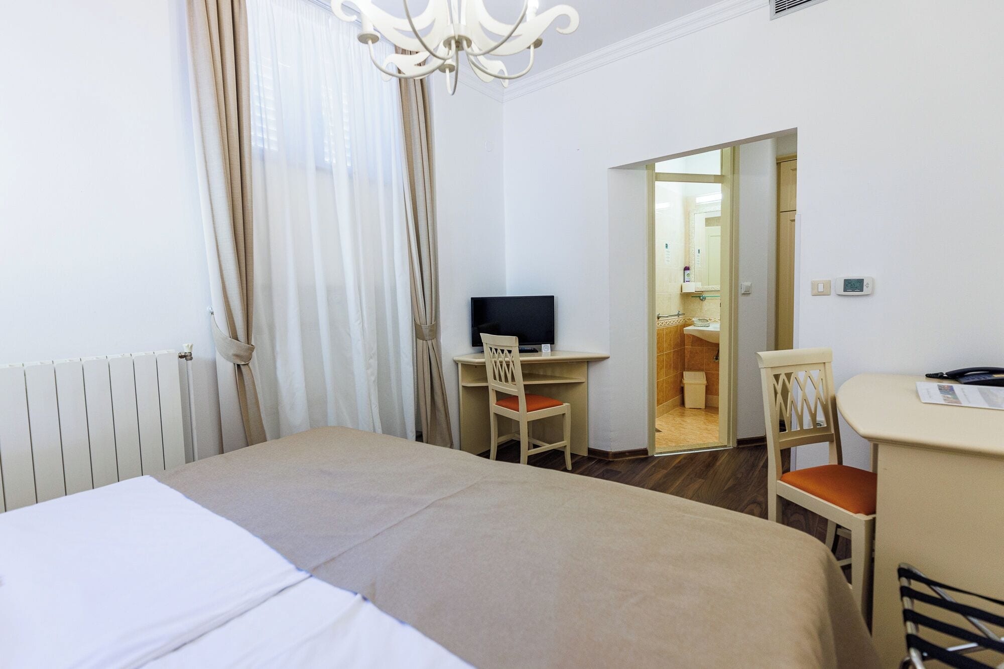 A hotel room with a bed, a desk with a computer, a chair, a small table, and a mirror.