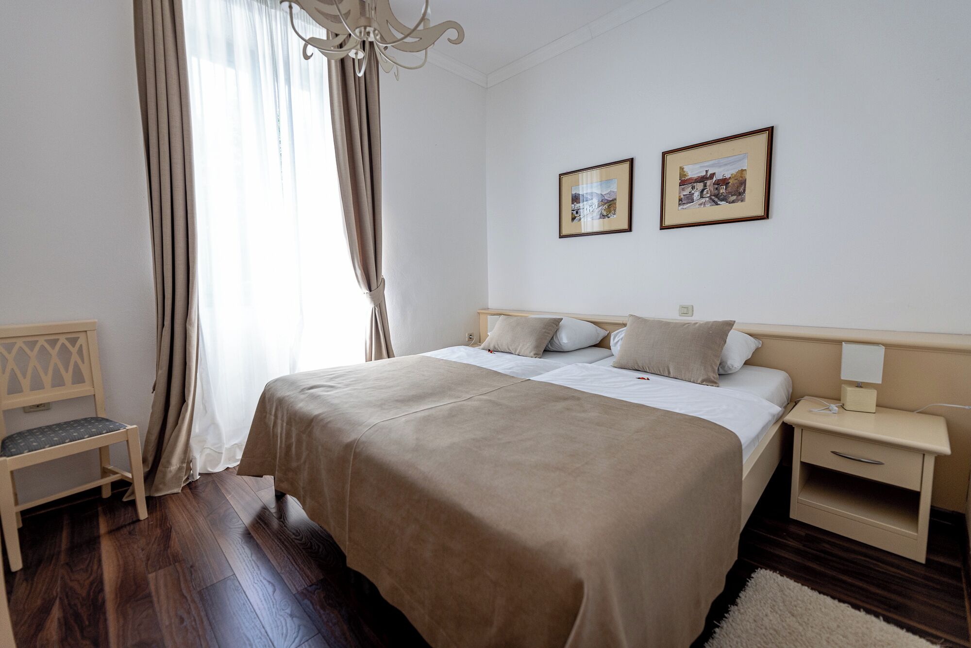 Ein ordentlich eingerichtetes Schlafzimmer mit einem großen Bett, einem Nachttisch, einem Sessel und zwei gerahmten Bildern an der Wand.