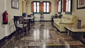 Amplia sala de estar con techo alto, vigas de madera, un extintor, una mesa de comedor, sillas, un sofá y una planta en maceta.