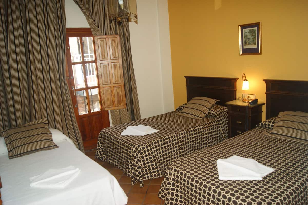 A hotel room with two beds, a wooden wardrobe, a nightstand with a lamp, and a framed picture on the wall.