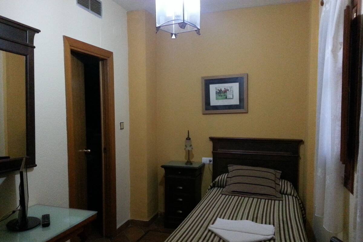 A small bedroom with a bed, a bedside table, a dresser, a mirror, and a picture on the wall.