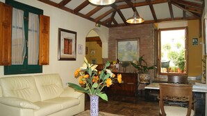 Una sala de estar con un sofá color beige, un florero azul con flores, vigas de madera en el techo y una pared de ladrillo.