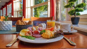 A breakfast table with a variety of foods, a potted plant, and a view of the outdoors. - Hotel Seeblick Wismar (Wismar)