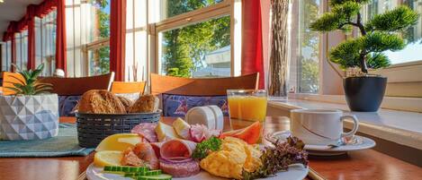 Een ontbijttafel met diverse soorten eten, een potplant en uitzicht op het buiten.