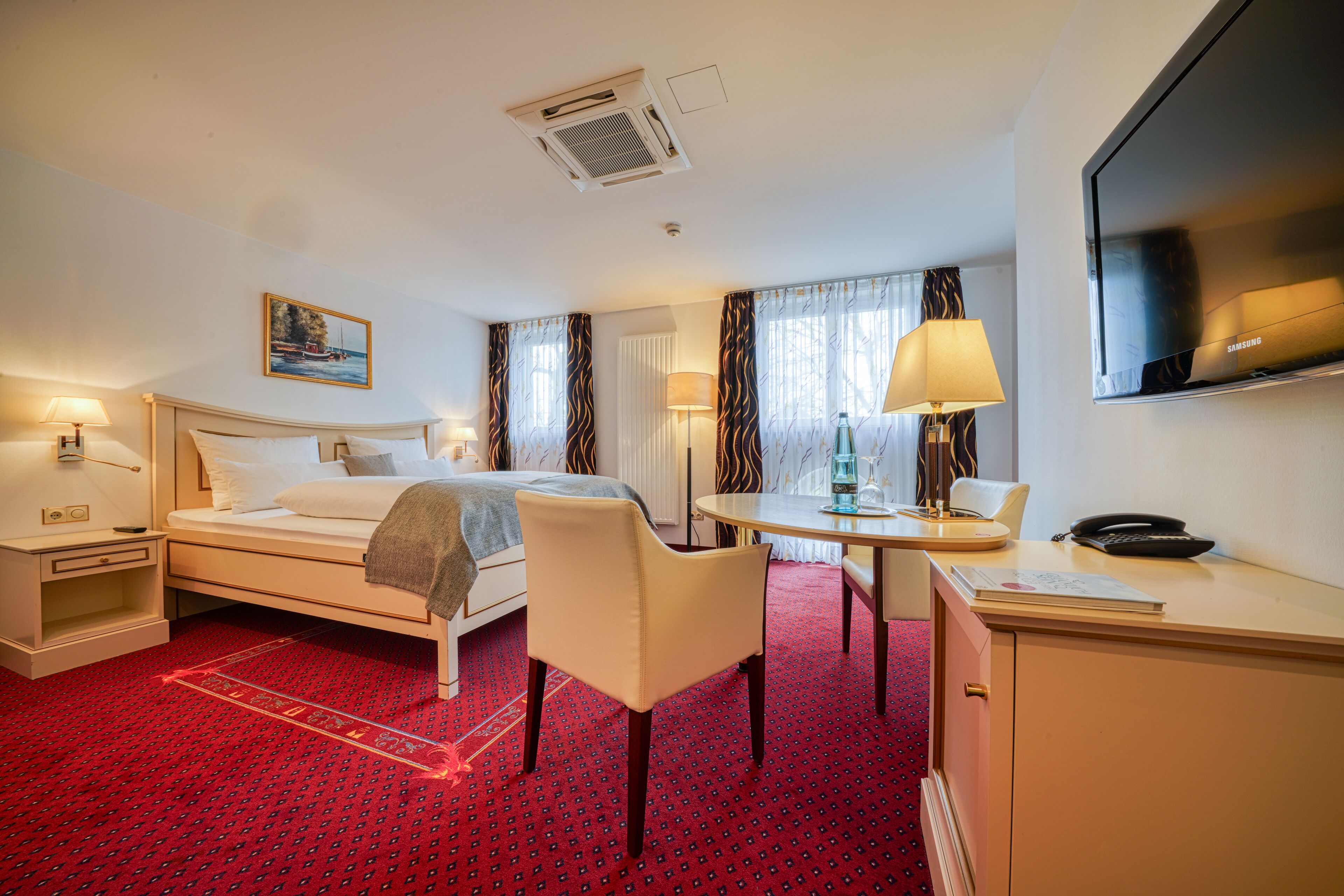 A hotel room with a bed, a desk, a chair, a TV, and a window with curtains.