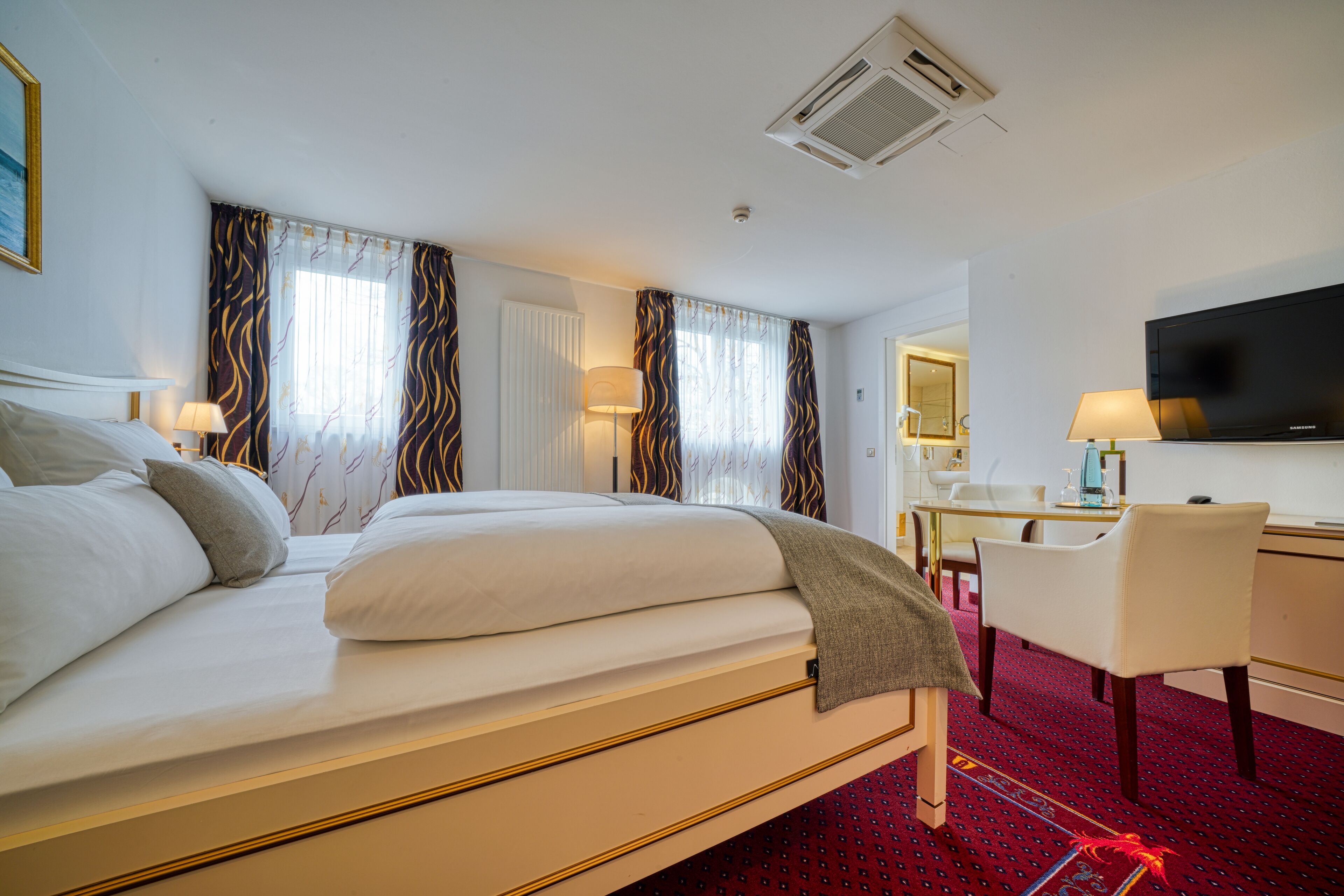 A hotel room with a large bed, a desk, a chair, a television, and curtains.