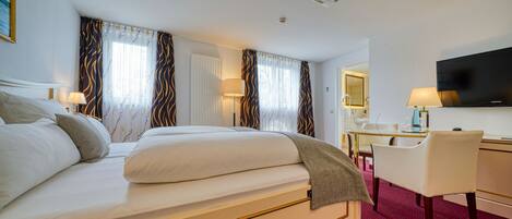 A hotel room with a large bed, a desk, a chair, a television, and curtains.